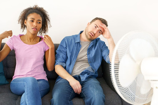 A woman and man stuggling to keep cool as they sit in front of a fan.