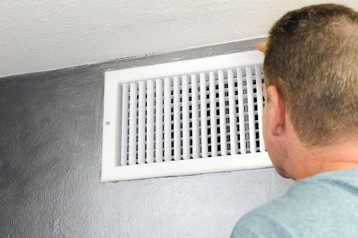 A man looking into an HVAC air duct.