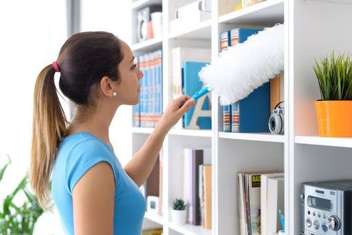 A woman dusting a bookcase in a home.